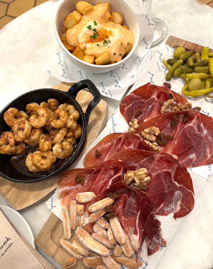 Grilled shrimp on a plate, charcuterie board of ham, and bowl of potatoes with spicy sauce